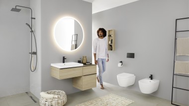 Homme entrant dans une salle de bains équipée d‘un lavabo, d‘un WC, d’un bidet et de meubles de la collection Geberit iCon. Homme entrant dans une salle de bains équipée d‘un lavabo, d‘un WC, d’un bidet et de meubles de la collection Geberit iCon.