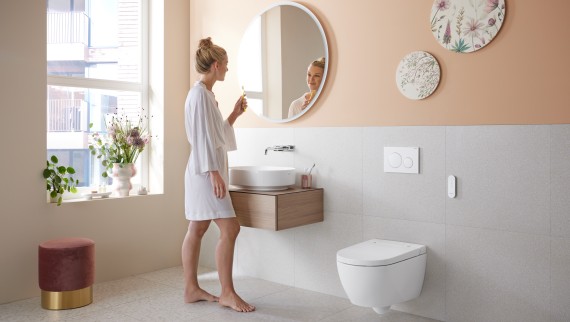 Femme dans une salle de bains dotée d’un Geberit AquaClean Alba – un WC économique avec fonction douchette Femme dans une salle de bains dotée d’un Geberit AquaClean Alba – un WC économique avec fonction douchette