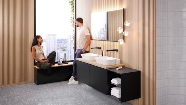 Femme assise sur le rebord d‘une fenêtre parlant à un homme dans une salle de bains Geberit ONE