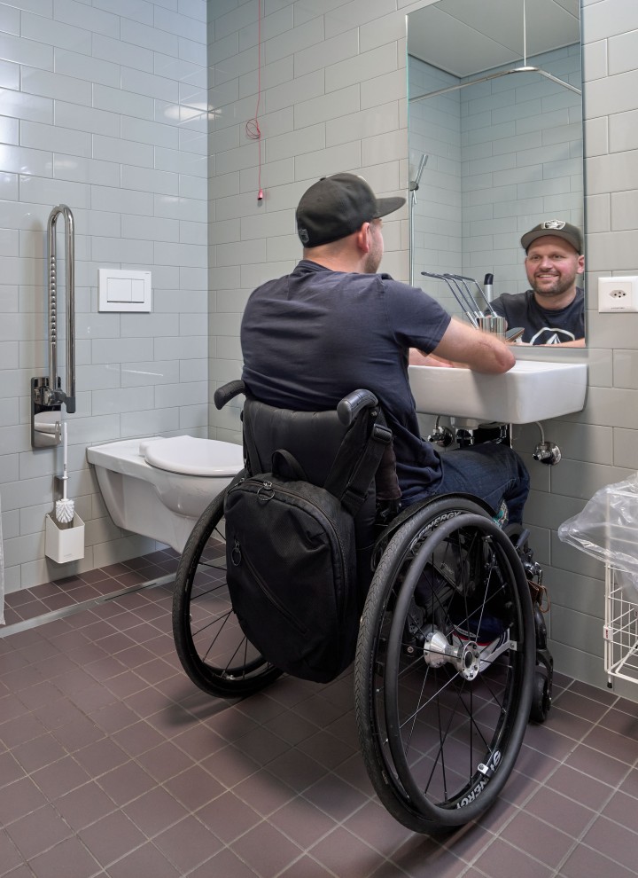 Peter Roos in een rolstoel bij de wastafelopstelling in een drempelloze badkamer (© Ben Huggler)