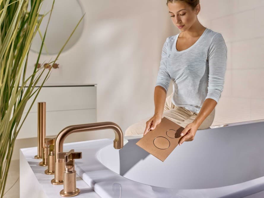 Vrouw in de badkamer met bedieningsplaat Sigma40 in de kleur geborsteld koper, die qua kleur afgestemd is op de kranen Vrouw in de badkamer met bedieningsplaat Sigma40 in de kleur geborsteld koper, die qua kleur afgestemd is op de kranen