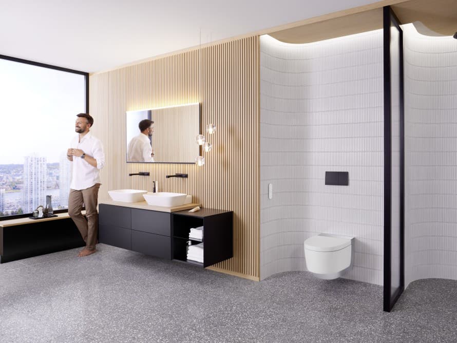 Man in een grote badkamer met donkere meubels en een Geberit AquaClean douche-wc Man in een grote badkamer met donkere meubels en een Geberit AquaClean douche-wc